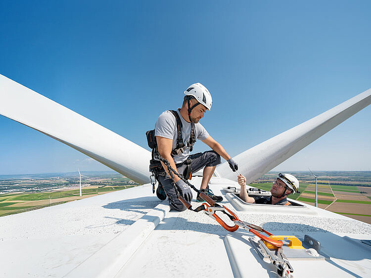 Two JUWI employees are working on a wind energy plant. The sky is bright blue.