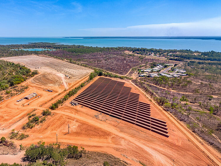 A solar park is located in close proximity to a residential area. On the horizon, the azure blue ocean shimmers.
