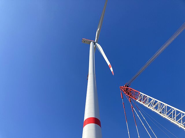 View from below of a wind turbine, next to it a crane in position.