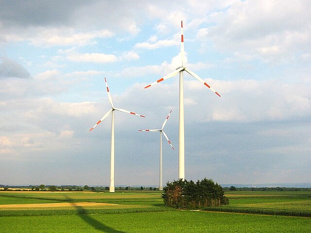 Auf einem offenen Feld sind drei Windenergieanlagen.