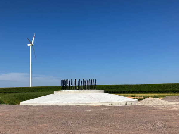 In a field, there is a wind turbine that has already been erected and the foundation for a wind turbine that is yet to be erected.